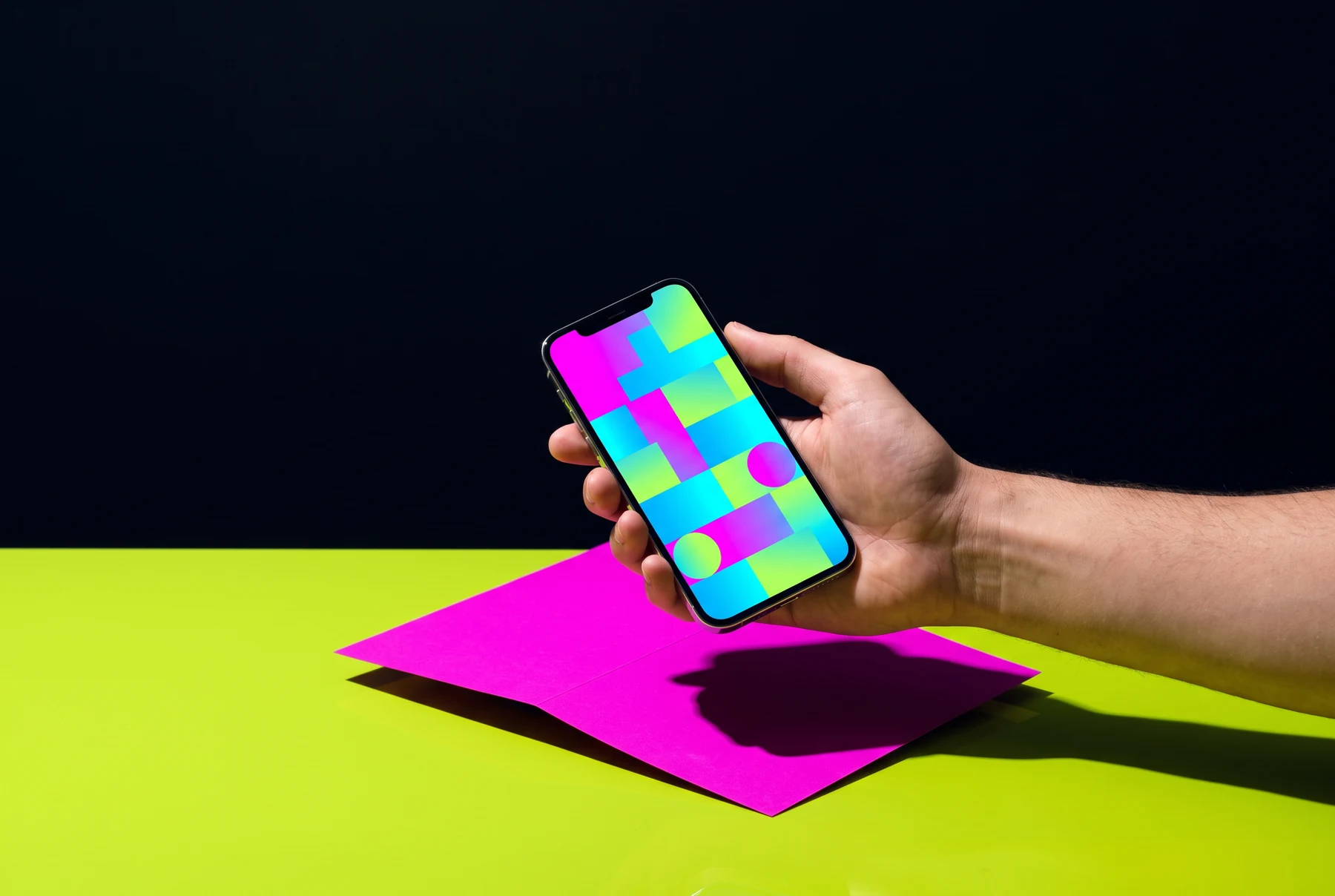 Hand holding a smartphone with an abstract colourful screen over a lime and pink desk